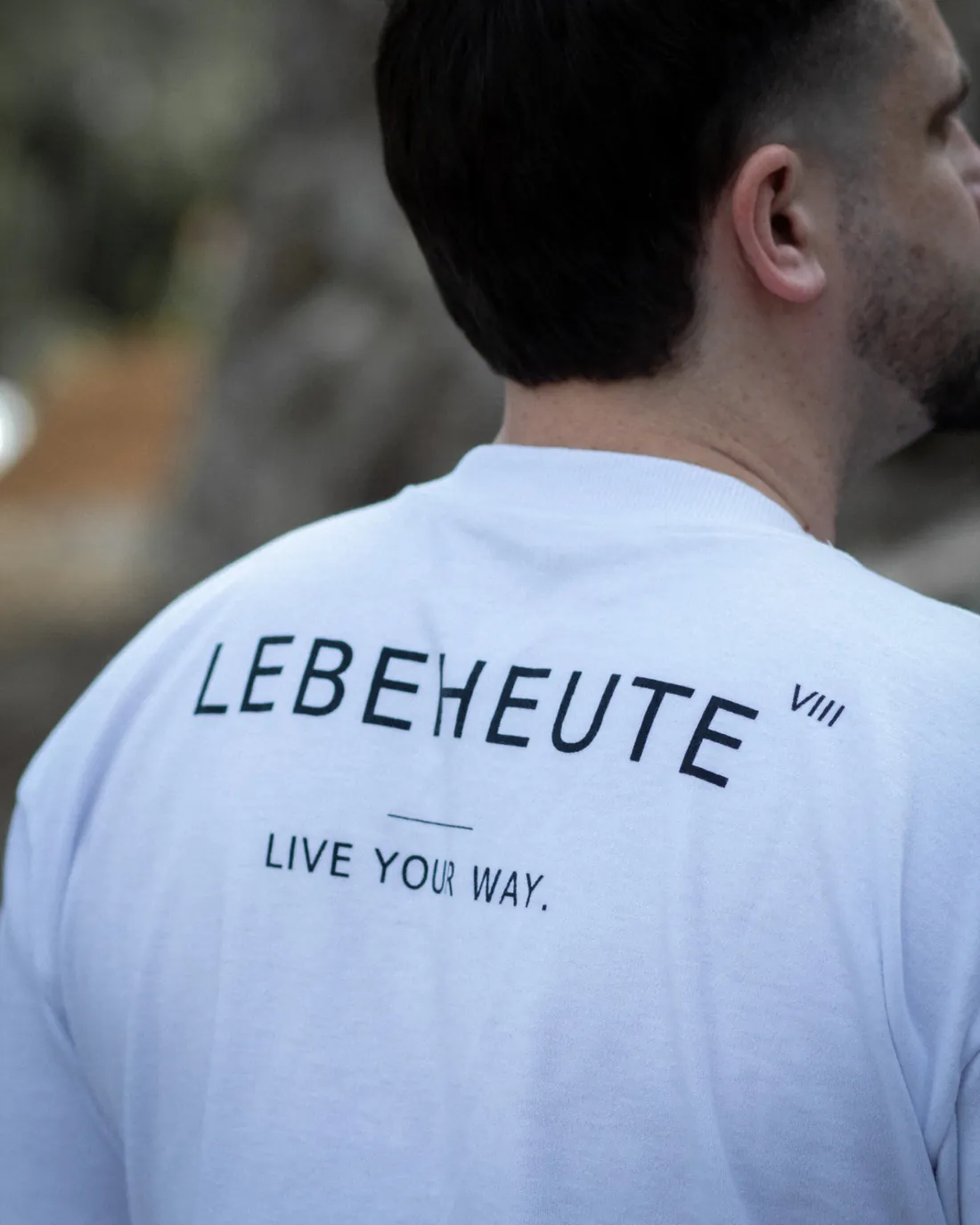 Detalhe da assinatura LEBEHEUTE VIII e do slogan na camiseta branca